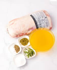 Seasoned pork roast in a slow cooker with herbs and broth for copycat Chipotle carnitas.