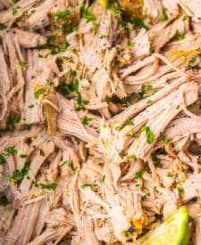 Tender shredded pork carnitas cooking in a slow cooker.