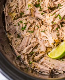 Tender shredded pork carnitas cooking in a slow cooker.