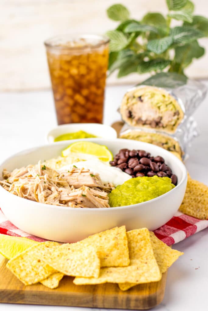 Slow cooker carnitas bowl served with rice, beans, and lime wedges.
