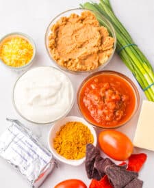 Ingredients for patriotic taco dip including beans, salsa, cheese, and sour cream.