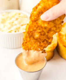 Close-up of crispy Raising Cane's style chicken tender dipped in homemade Cane's sauce.