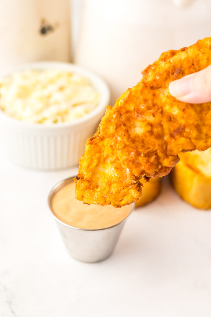 Close-up of crispy Raising Cane's style chicken tender dipped in homemade Cane's sauce.