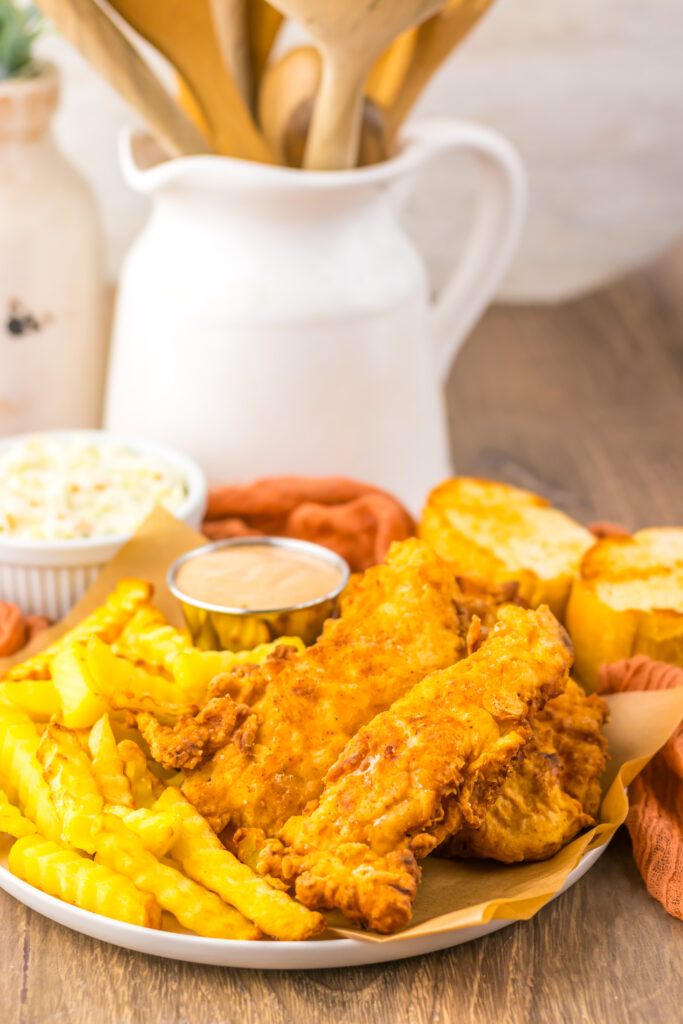 Plate of crispy chicken tenders with fries and homemade Cane's sauce.