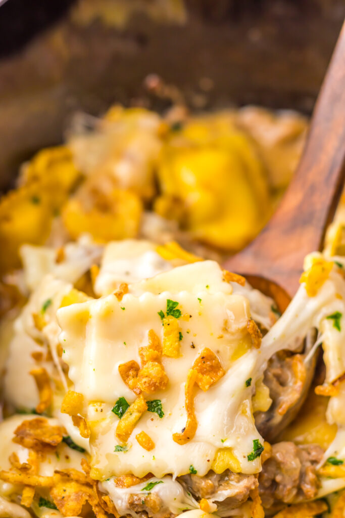 Wooden spoon serving creamy French Onion Ravioli from the slow cooker.