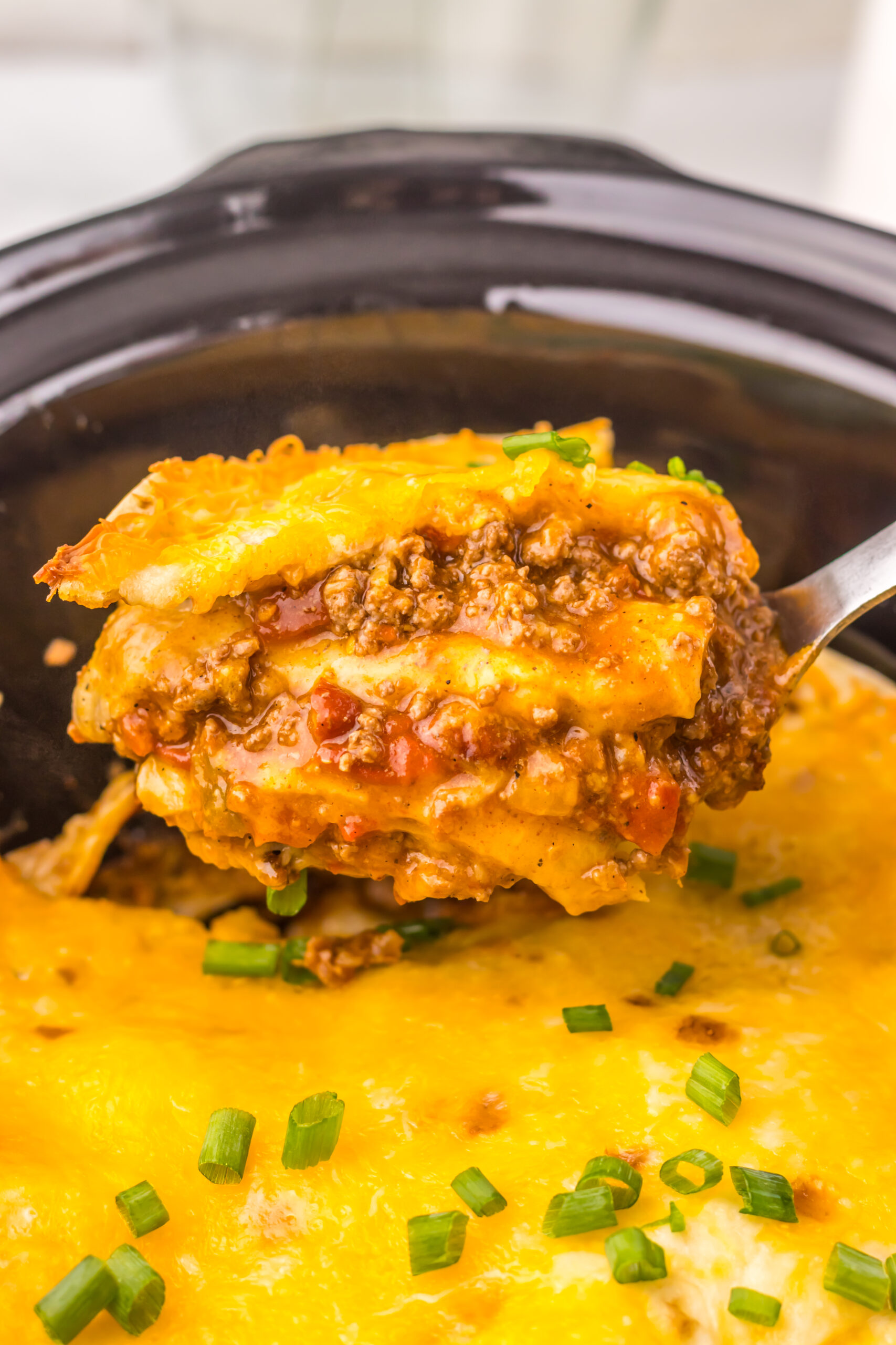 Spoonful of Slow Cooker Chili Cheese Enchilada Bake showing layers of beef, tortillas, and melted cheese.