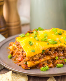 Finished Slow Cooker Chili Cheese Enchilada Bake with beef, tortillas, melted cheese, and green onions.