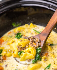 Ladle scooping creamy tortellini soup from the slow cooker.