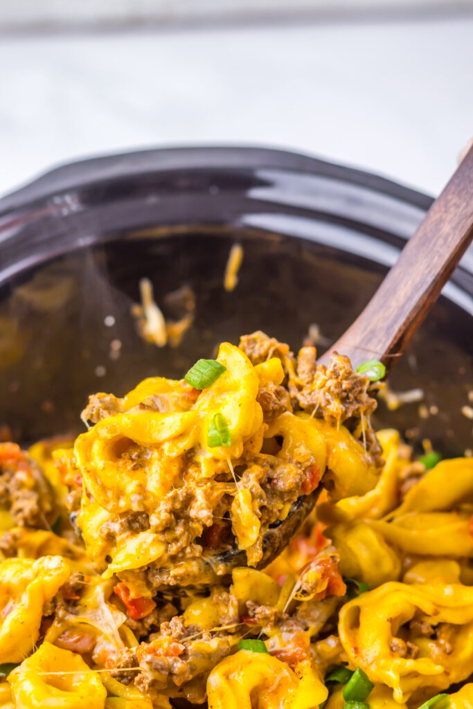 Slow Cooker Taco Tortellini being served from the crockpot with melted cheese and seasoned beef.