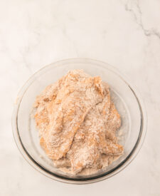 Raw chicken breast coated in seasoned flour for a crispy spicy chicken sandwich.