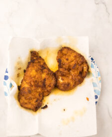 Crispy golden brown spicy chicken fillets resting on a paper towel after frying.