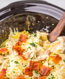 Slow Cooker Crack Chicken Alfredo Ravioli being stirred together with a wooden spoon.