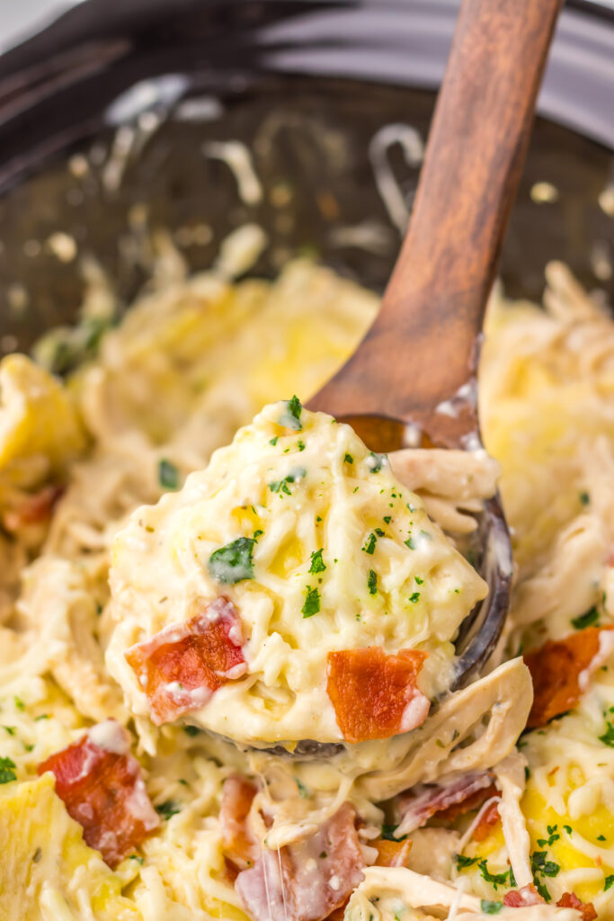 Creamy cheese ravioli and chicken being scooped from the slow cooker.