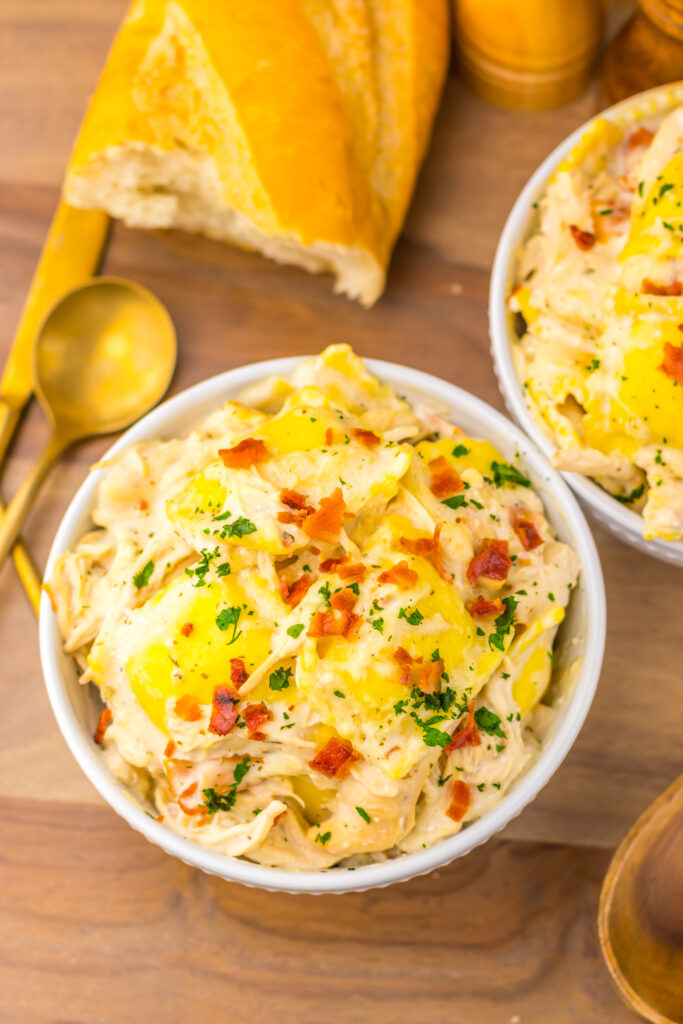 Overhead view of Slow Cooker Crack Chicken Alfredo Ravioli with cheesy bread and seasonings.
