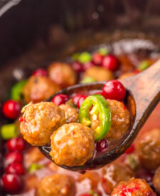 Slow Cooker Cranberry Jalapeño Meatballs being stirred with a wooden spoon.