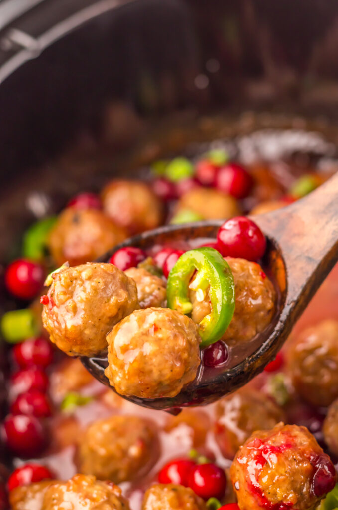Slow Cooker Cranberry Jalapeño Meatballs being stirred with a wooden spoon.